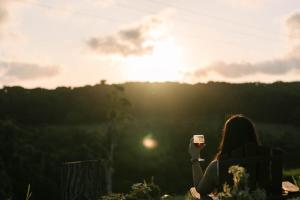 a woman holding a cup of coffee in front of the sunset at Rainforest Sunsets by Tiny Away in Kuranda