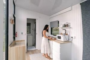 a woman standing in a kitchen with a microwave at Rainforest Sunsets by Tiny Away in Kuranda +6 photos
