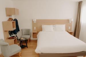 a bedroom with a large white bed and a chair at Kyriad Quimper Sud in Quimper
