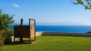 a statue sitting in the grass near the ocean at Panoramic Sea View Wooden Cottage Ratzakli, Kefalonia in Ratzaklíon