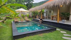 a person sitting next to a swimming pool next to a house at Amed Saïta Villas in Amed