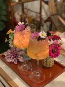 three cocktails sitting on a wooden tray with flowers at กลิ่นไอทุ่งโฮมสเตย์ in Ban Thum +18 photos