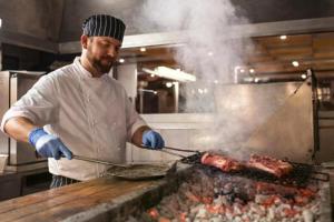 a man cooking meat on a grill in a kitchen at Hotel Kursaal in Rimini