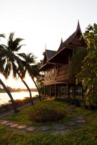 a wooden house with palm trees in front of the water at RK Riverside Resort & Spa (Reon Kruewal) in Ban Khlong Krang