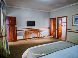a bedroom with a bed and a desk with a television at Phumulani Lodge Kameeldrift in Pretoria
