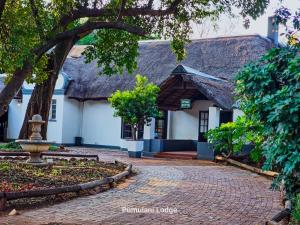 a building with a thatched roof and a brick walkway at Phumulani Lodge Kameeldrift in Pretoria +16 photos