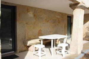 a white table and two stools next to a stone wall at Recanto da Malhadoira in Currais