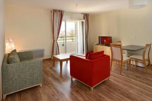 a living room with a red chair and a table at Domitys Le Côteau d'Argent in Saint-Doulchard