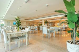 a restaurant with white tables and chairs and plants at Mövenpick Hotel & Resort Al Bida'a in Kuwait
