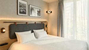 a bedroom with a bed with white pillows and a window at Campanile PRIME - Paris 15 Tour Eiffel in Paris