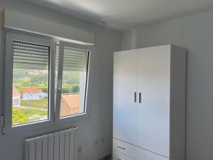 a room with a white cabinet and two windows at Apartamentos Vive Laxe in Laxe