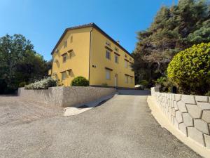 a yellow house with a stone wall next to a road at Apartment Gracia 1 in Baška