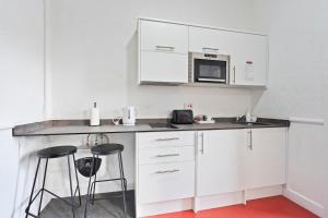 a kitchen with white cabinets and a microwave and stools at Modern Self-Contained Studio in Dudley Sleeps 2 in Dudley