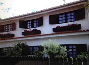 a white building with red flowers in windows at Casa de praia com piscina in Árvore