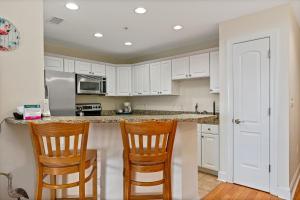 a kitchen with white cabinets and two chairs at Dreamer by Oak Island Accommodations in Oak Island