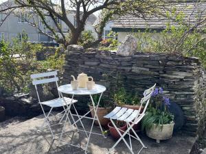 a table and chairs in front of a stone wall at Sunnybrae Cottage in Tintagel