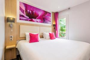 a bedroom with a large white bed with pink pillows at FH Confort Hotel Orléans Co'met in Orléans