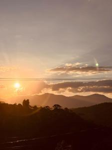 a sunset with the sun setting over the mountains at Refugio nas Alturas LANDIN & CHARM in Santo Antônio do Pinhal