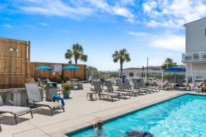a pool with chaise lounge chairs and a man standing on a patio at The Island Sandpiper by Oak Island Accommodations in Oak Island