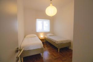two beds in a room with a window and a lamp at Casa do Largo Ericeira in Ericeira