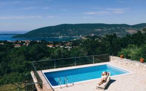 a person sitting in a chair next to a swimming pool at Vila Bella Vista in Herceg-Novi