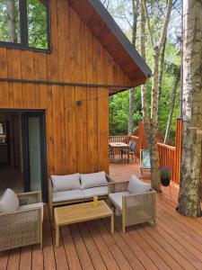 a patio with couches and a table on a wooden deck at Dadaj Chill 2 domek nad jeziorem, wanna jakuzzi, fotel masujący in Wilimy