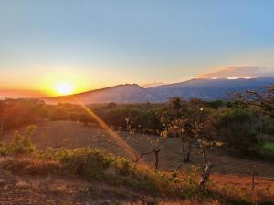 a sunset over a field with mountains in the background at Hospedaje La Guaca in Bagaces