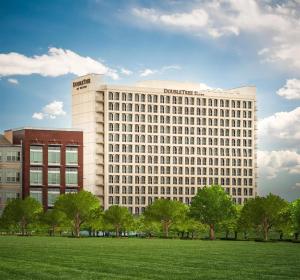 a large white building with trees in front of a field at DoubleTree by Hilton Dallas Market Center in Dallas