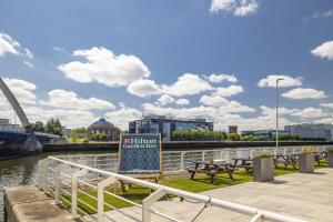 a sign next to a river with benches and a bridge at Hilton Garden Inn Glasgow City Centre in Glasgow