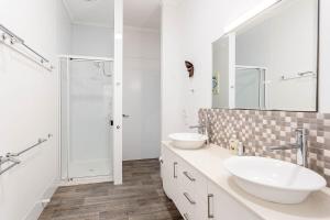 a white bathroom with two sinks and a shower at Sunrise on the Esplanade in Yeppoon