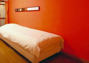 a bed in a room with an orange wall at ゲストハウス303 in Zamami