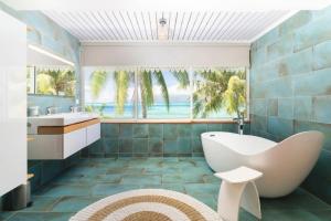 a bathroom with a tub and a sink and palm trees at Luxurious 4BR Villa in Vairoa