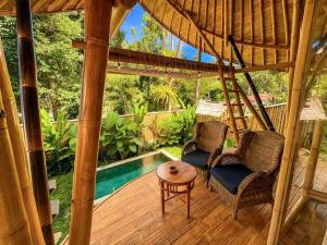 a porch with two chairs and a table and a pool at Hidden Bamboo Village in Sidemen