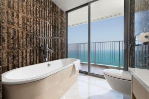 a bathroom with a tub and a toilet and large windows at Wyndham Soleil Danang - Free Schedule Airport Shuttle in Danang