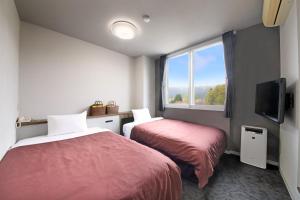 two beds in a room with a window and a tv at Gogaku Hotel in Aso
