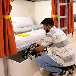 a man sitting on the floor next to a bed at Metro POD Hotel at New Delhi Metro & Railway Station in New Delhi