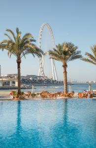 a pool with palm trees and a ferris wheel in the background at DoubleTree by Hilton Dubai Jumeirah Beach in Dubai