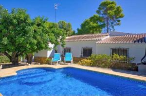 a swimming pool with two blue chairs and a house at villa cap marti in El Tosalet