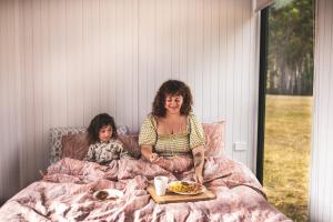 a woman and a child sitting in bed with a plate of food at Pine Edge Heights by Tiny Away in Ellendale