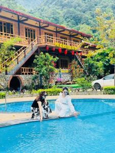 two women sitting on the edge of a swimming pool at Pác Bó Boutique Hotel in Cao Bằng