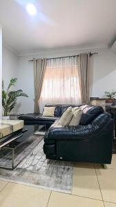 a living room with a black leather couch in front of a window at Vine Vale in Kampala