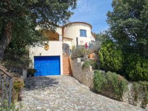 a house with a blue garage door on a stone driveway at Casa Mimosa, Calonge Cabanyes in Calonge