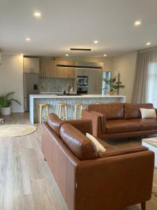 a living room with two brown leather couches and a kitchen at The Batch in Oamaru
