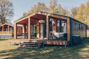 a wooden cabin with a deck and chairs in a field at Resort Wilsumer Berge in Wilsum