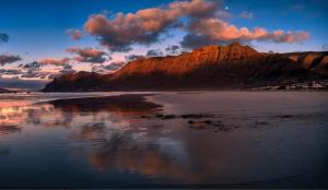 a mountain reflecting in the water on a beach at Bungalow Olas del Risco - Ocean views - Beach 2 min By Lanzarote Vacation Homes in Famara