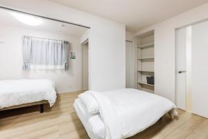 two beds in a bedroom with white walls and wooden floors at Anecis笠取町2 in Nagoya