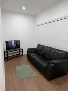 a black leather couch in a living room with a tv at Second Home - A modern 4 Bedrooms House in Blacktown
