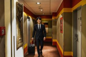 a man in a suit walking down a hallway with a suitcase at Afrika Hotel Frýdek-Místek in Frýdek-Místek
