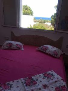 a bed with a purple comforter and a window at Haouaria PANTELLERIA in Sidi Amor