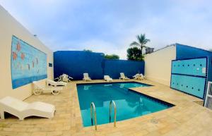 a swimming pool with white chairs and a blue wall at Hotel Caiçara in Praia Grande